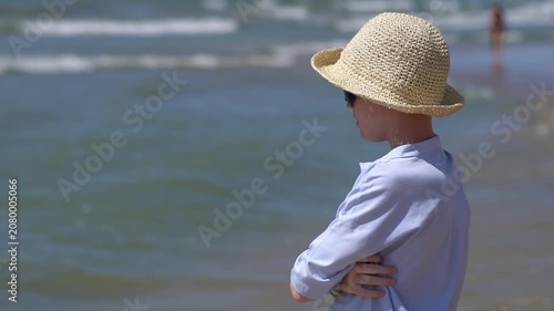 A teenager wearing a hat stands on a tropical island beach, admiring the sunset. A peaceful summer getaway or vacation; summer travel concept.