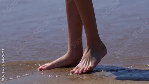 Teenage girl's legs on the beach, small gentle waves covering the child's legs, the child playing with the waves
