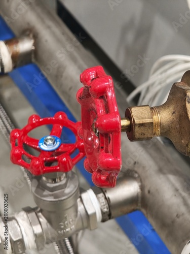 A close-up view of two red handwheel valves connected to brass and stainless steel pipes in a factory