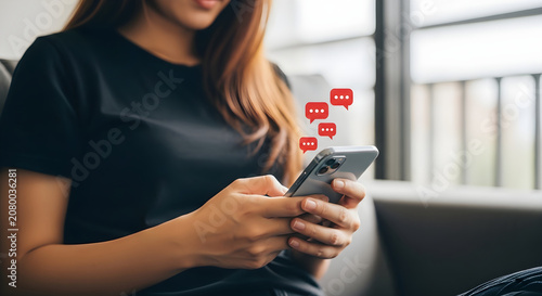 Woman sitting on sofa uses smartphone with social media notifications.