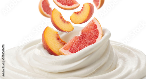 Distant shot of peach and grapefruit slices falling into thick whipped cream with a clean splash
