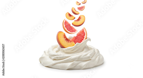 Distant shot of peach and grapefruit slices falling into thick whipped cream with a clean splash