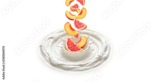 Distant shot of peach and grapefruit slices falling into thick whipped cream with a clean splash