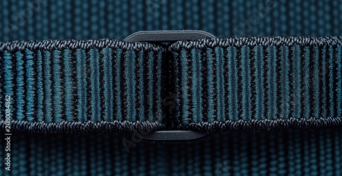 Macro view of teal ribbed nylon strap threaded through a black plastic buckle, tight stitching and a secure utilitarian feel