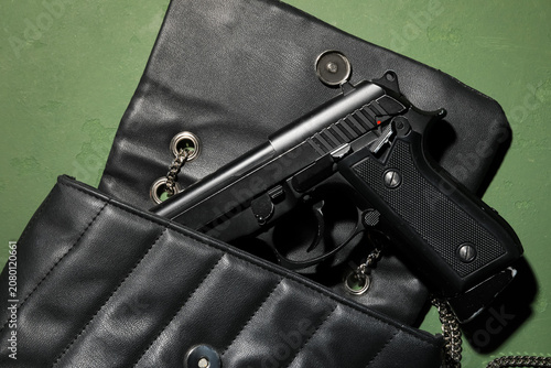 Canvas Print Black handgun in black leather purse on green surface