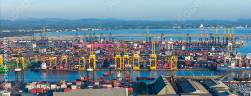 commercial port terminal with cargo ships, container stacks, gantry cranes, storage warehouses, and large car parking lots facilitating global maritime trade and logistics supply chain.