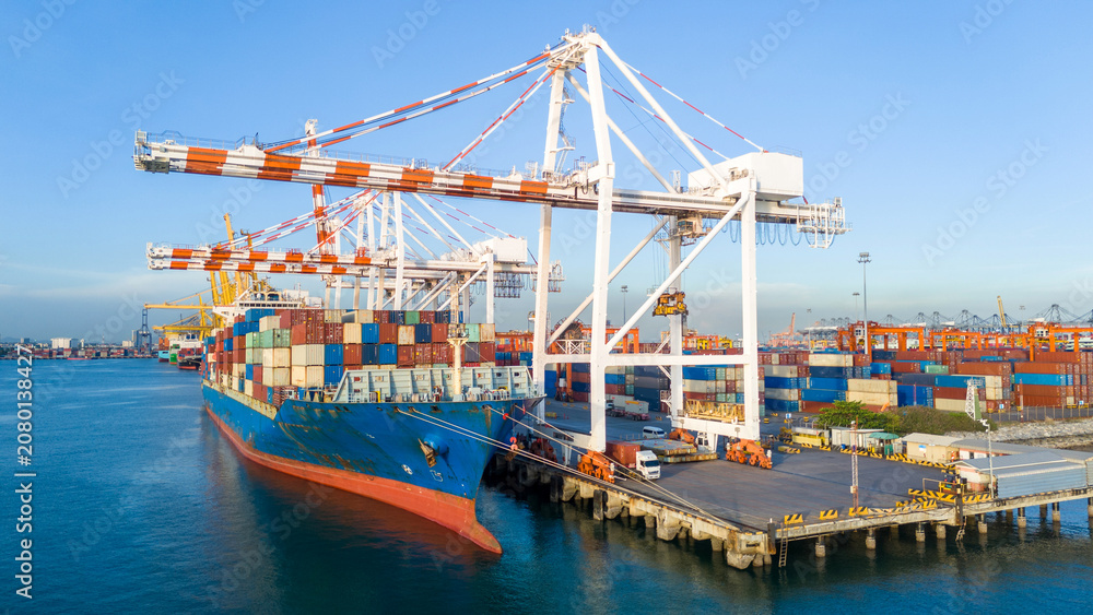 Naklejka premium cargo container ship docked at a commercial port terminal with giant gantry cranes loading freight, representing global maritime logistics, supply chain, and international trade.