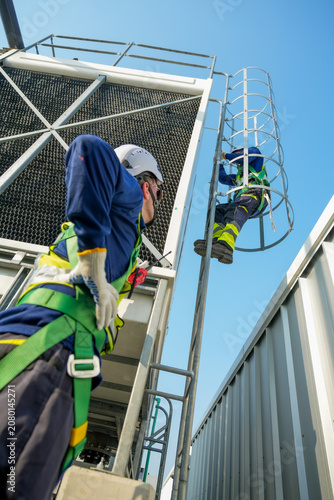 Engineer ascending cooling tower ladder. Rooftop HVAC system maintenance, industrial worker inspecting cooling unit for optimal performance.