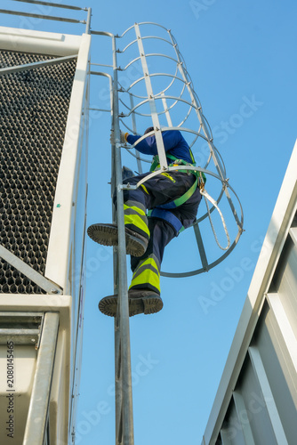 HVAC technicians perform cooling tower inspection. Rooftop maintenance, safety gear worn, industry professionals.