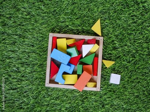Top down flat lay view of colorful geometric wooden building blocks inside a tray on artificial green grass.