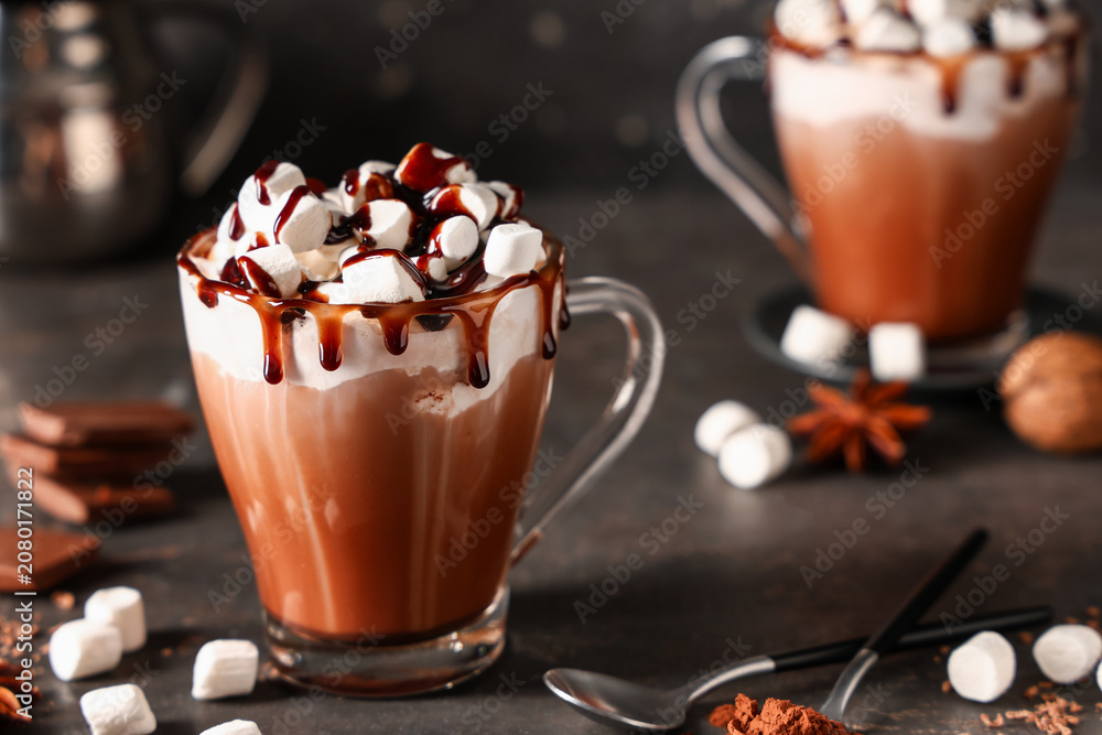 Fototapeta premium Glass cup of hot cocoa drink with whipped cream, marshmallows and liquid chocolate on dark background