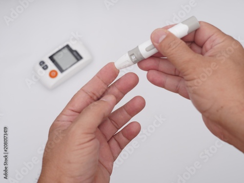 Fotografie Close-up of a person using a blood glucose lancing device for a fingertip blood sugar test with a digital glucose meter in the background