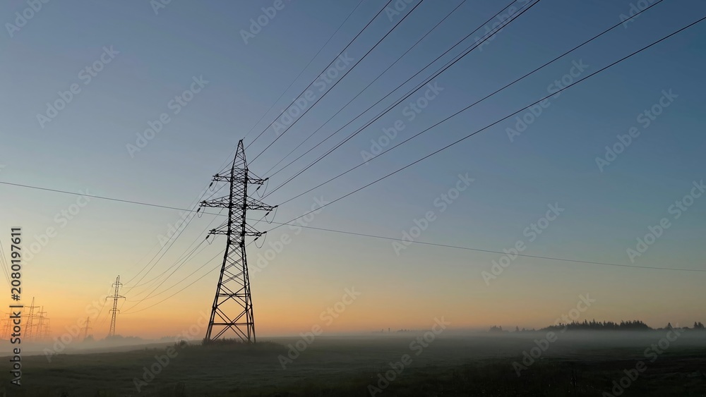 Fototapeta premium High voltage power transmission lines at sunrise with morning fog, electricity pylons across rural landscape, energy infrastructure, scenic industrial background