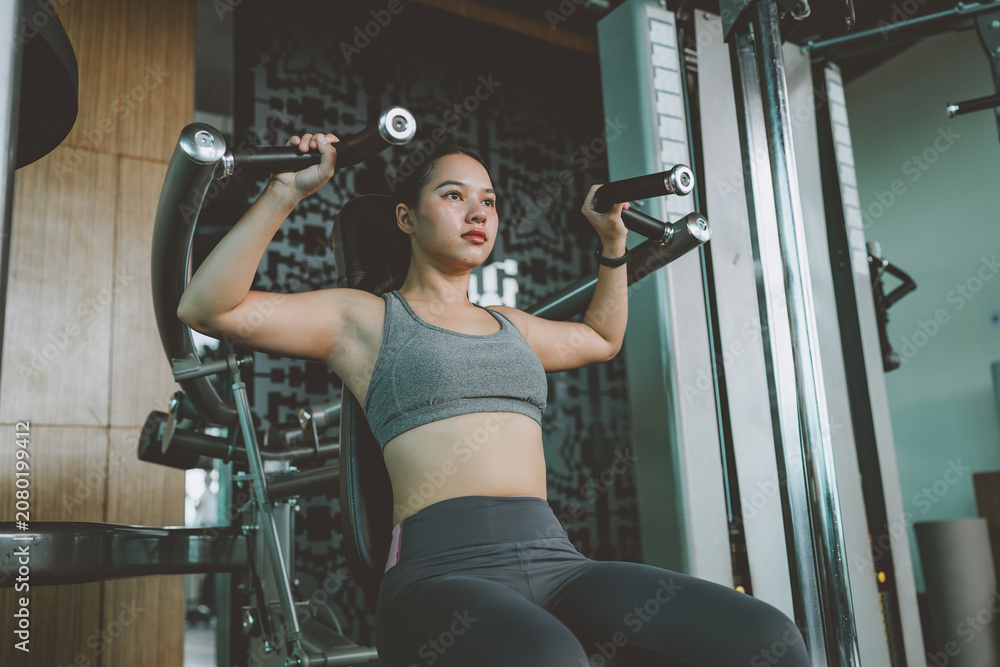 Fototapeta premium Woman exercising on shoulder press machine in gym