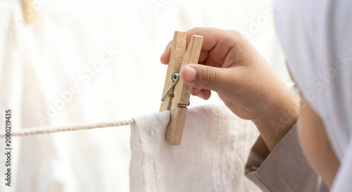 Close up of a hand using a wooden clothespin to hang white laundry on a clothesline