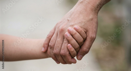 Close up of an adult holding a small child hand outdoors with blurred background