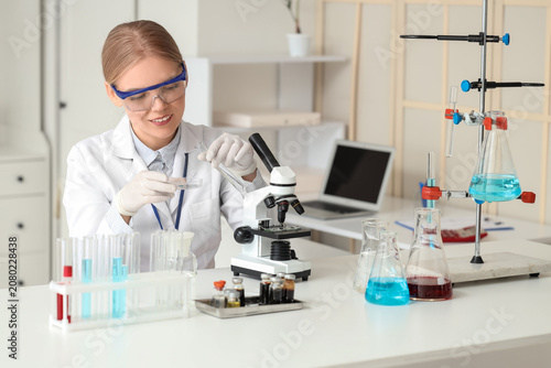 Female scientist with glassware and microscope working at table in laboratory