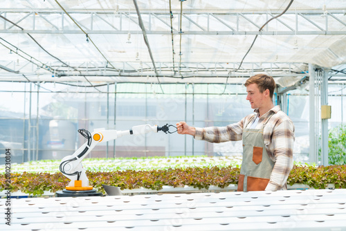 Smart farmer fist bumping collaborative robotic arm in hydroponic greenhouse demonstrating human robot collaboration agricultural automation smart farming innovation and sustainable food production