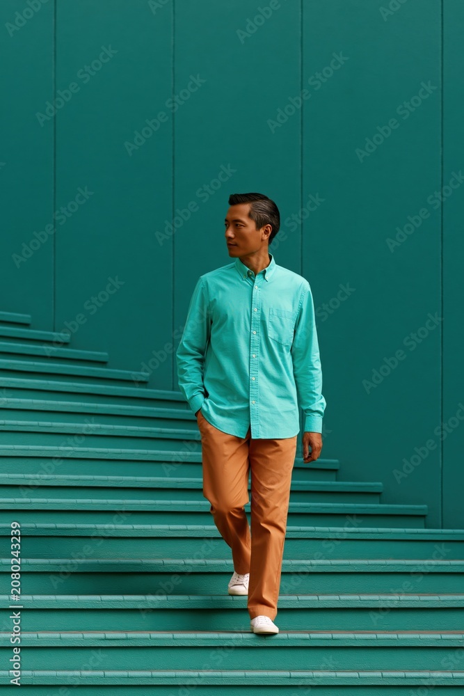Obraz premium Male model walking down teal stairs in turquoise shirt and orange trousers for fashion lifestyle background and banner design