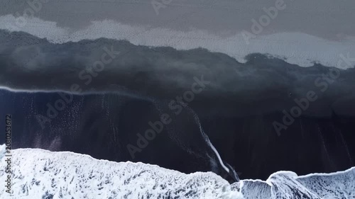 Aerial view of white ocean waves crashing on dark black sand beach