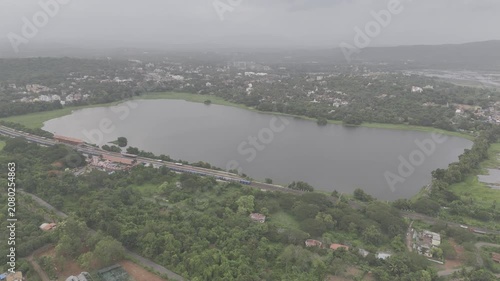 Aerial view of a train at Karmali Railway Station near Carambolim Lake in Old Goa, surrounded by lush greenery, coconut palms, and trees beneath cloudy monsoon evening skies.
