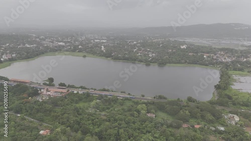 Aerial view of a train at Karmali Railway Station near Carambolim Lake in Old Goa, surrounded by lush greenery, coconut palms, and trees beneath cloudy monsoon evening skies.