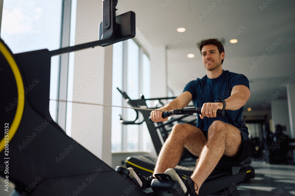 Fototapeta premium Close up of athlete working out on rowing machine in health club.