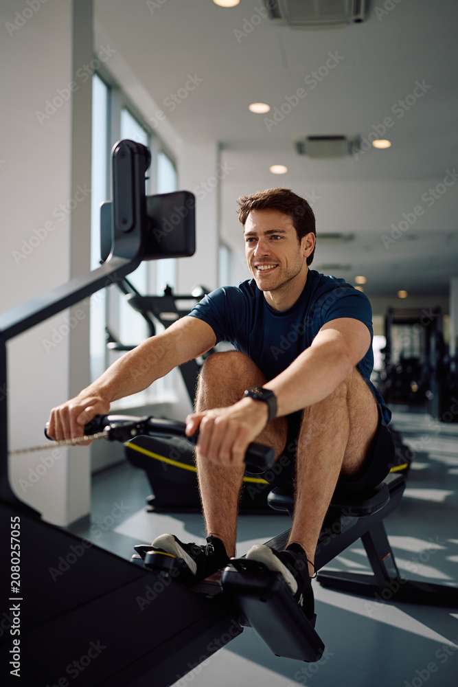 Obraz premium Happy sportsman exercising on rowing machine during gym workout.