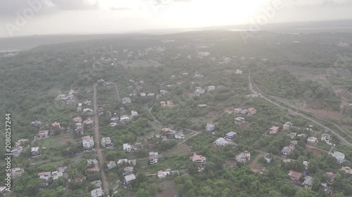 Aerial view of houses in Old Goa surrounded by lush greenery during the pre-monsoon season, with a dramatic sunset glowing through cloudy skies over the scenic landscape.