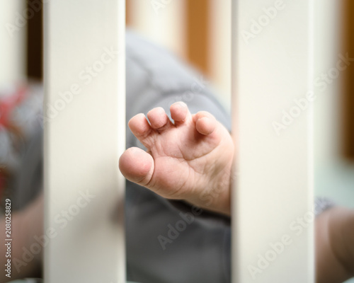 Tiny baby foot with five tiny toes says hello between the bars of the playpen