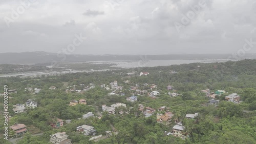 Aerial view of Old Goa and nearby houses along the Mandovi River during the monsoon season, featuring cloudy skies, lush surroundings, and the scenic riverside landscape of Goa.