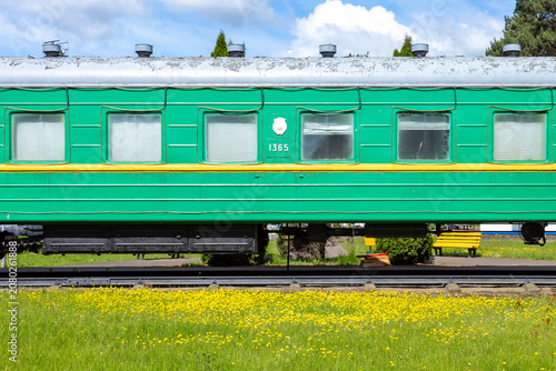 Quadro su tela A vintage emerald green passenger railcar rests statically along tracks bordered by a vibrant field of yellow wildflowers under a sky