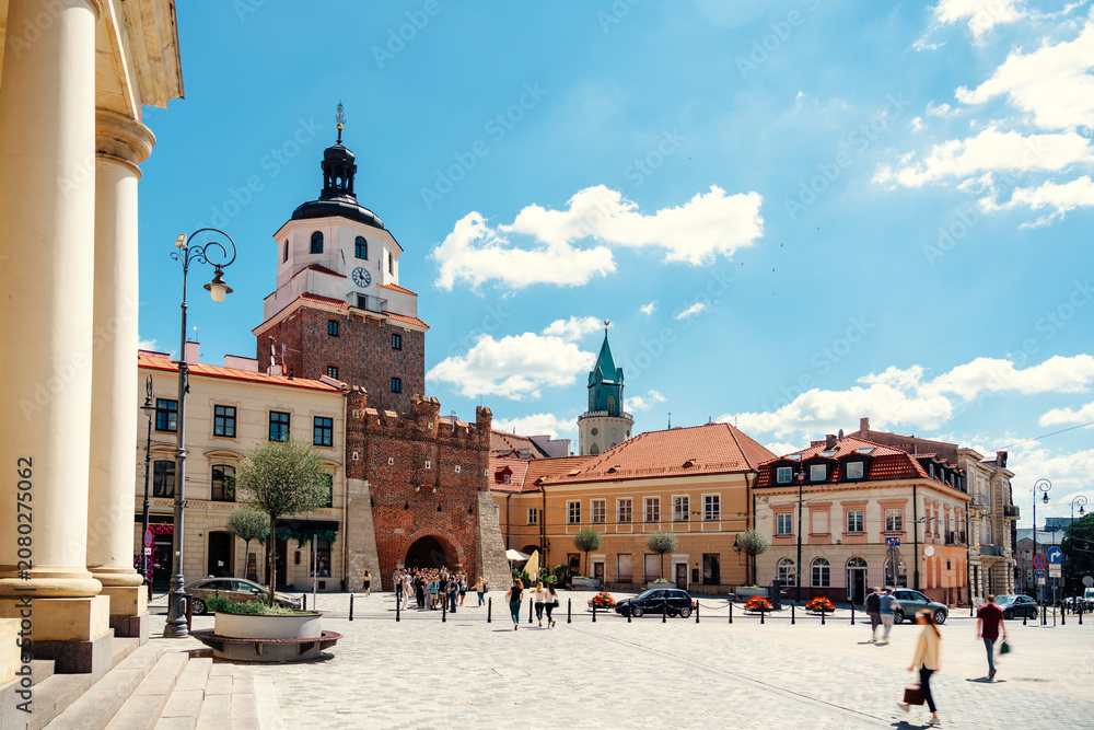 Obraz premium The historic Kraków Gate stands prominently as the gateway to the charming, sunlit Old Town square in Lublin, Poland.