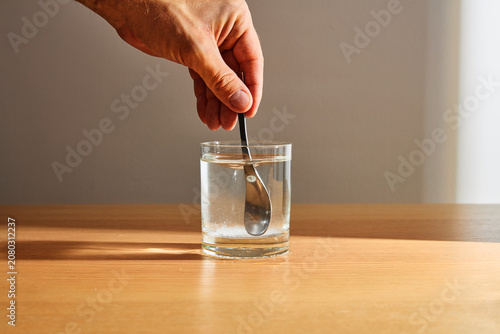Bild auf Leinwand Hand stirring soluble powder in glass of water with spoon on wooden table