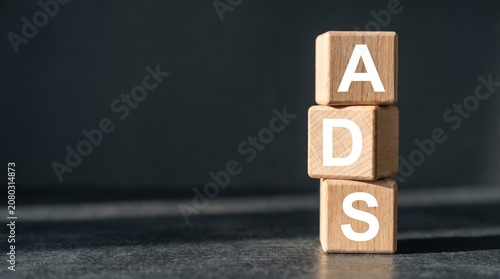 ADS word written on wooden blocks stacked vertically on a dark background, representing marketing and advertising concept.