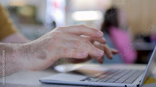 Close-up of hands typing on laptop keyboard. Person focused, working quietly in casual setting. Background blurred, suggesting cafe or office environment. Ideal for scenes of remote work