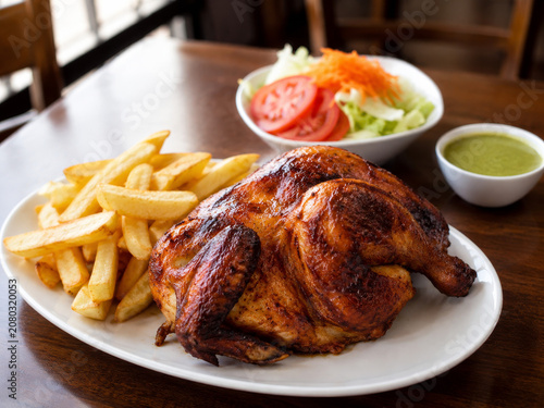  Pollo a la Brasa peruano servido con papas fritas, ensalada fresca y salsa cremosa de ají verde.