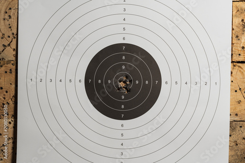 Fotografija Paper target with tight bullet holes group hanging on wooden bullet trap backgro