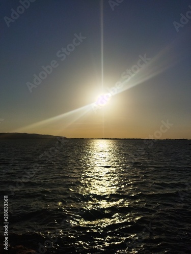 Atardecer con sol brillante y destellos dorados reflejados en el agua de la Laguna de Orbetello, Toscana, Italia.