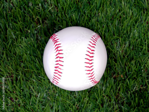 A white baseball with red stitching on the grass