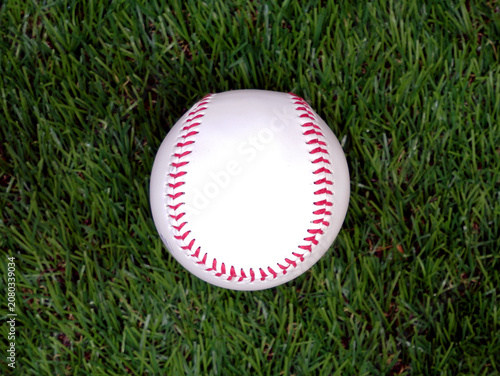 A white baseball with red stitching on the grass
