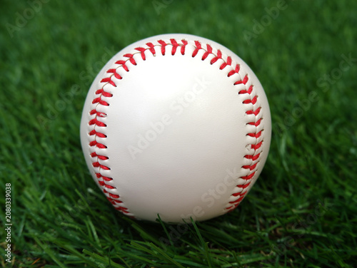 A white baseball with red stitching on the grass