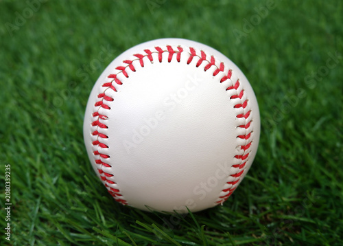 A white baseball with red stitching on the grass