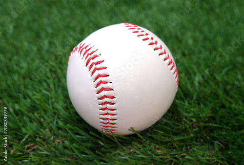 A white baseball with red stitching on the grass