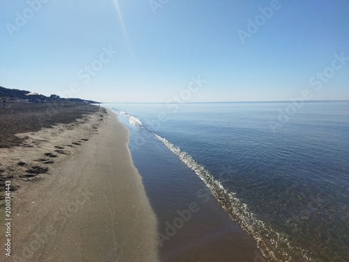 Línea de costa y orilla de una playa tranquila con aguas cristalinas bajo un cielo azul despejado, Toscana, Italia.
