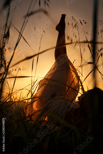 Barfüßige Frau entspannt in einer Blumenwiese bei Sonnenuntergang. Stimmungsvolles Lifestyle-Motiv zu Sommer, Freiheit, Natur, Achtsamkeit, Wellness, Entspannung und Slow Living.