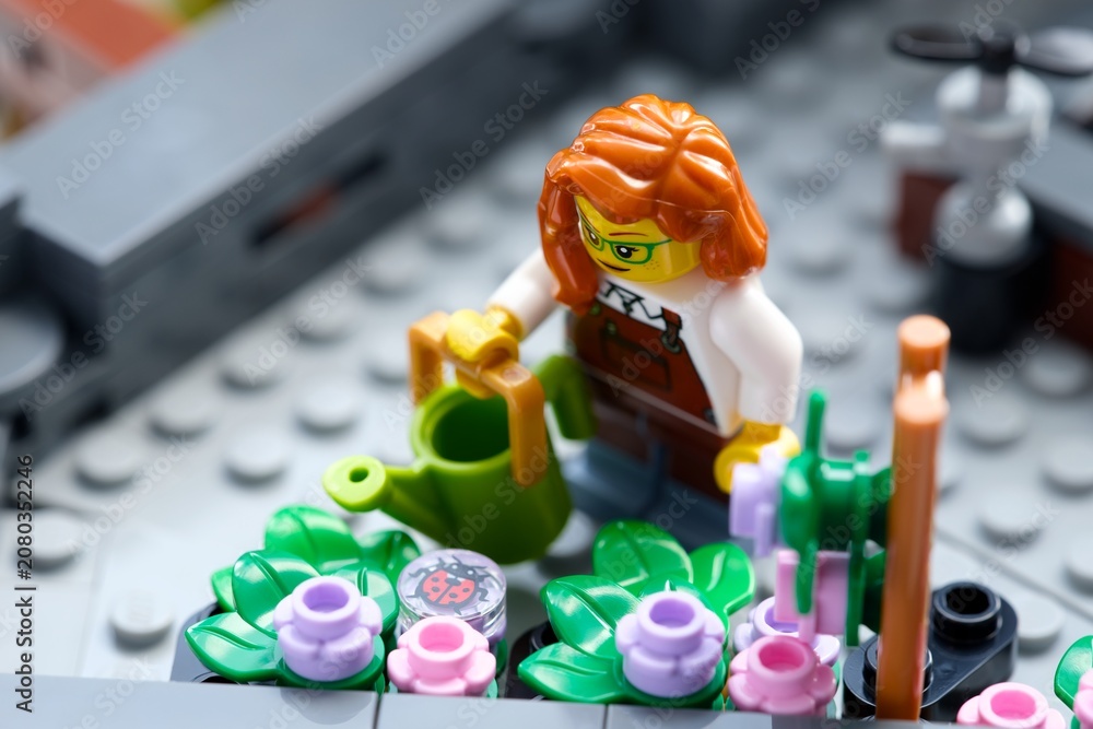Obraz premium Tambov, Russian Federation - June 24, 2026 A Lego woman gardener minifigure with a green watering can near a blooming flower bed on a city rooftop garden.