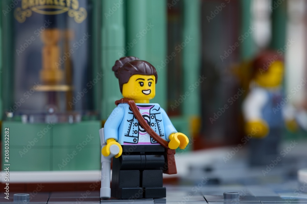 Obraz premium Tambov, Russian Federation - June 24, 2026 Lego woman minifigure with a crutch and a shoulder bag standing on a city street in front of a green building.