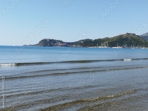 Vista panorámica de la costa y el puerto de Porto Ercole desde una playa de aguas tranquilas, Toscana, Italia.