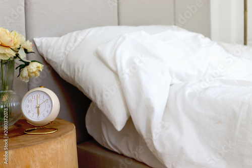 Canvas Print A vintage alarm clock on a bedside table next to a white bed in a cozy bedroom